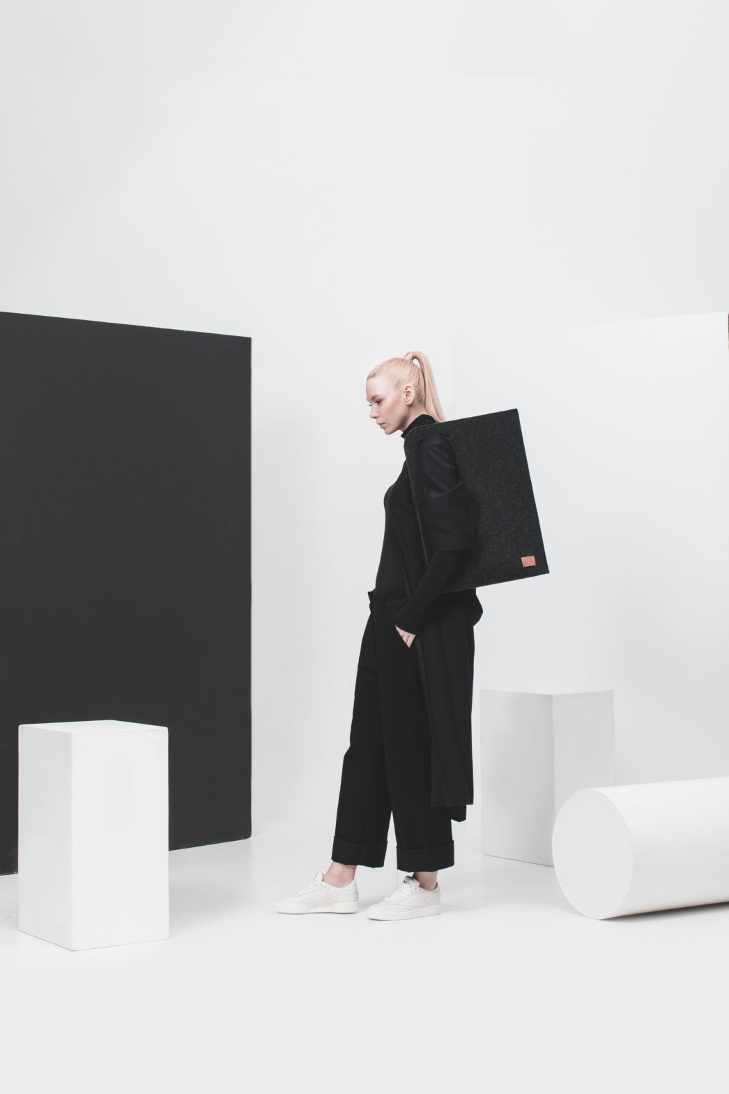 Woman dressed in black carrying the black Nord tote in a minimalist white studio.
